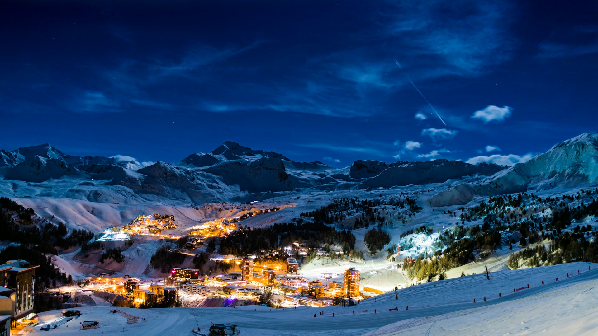 Beste skigebieden Frankrijk met verlicht skidorp en besneeuwde bergtoppen onder een heldere sterrenhemel