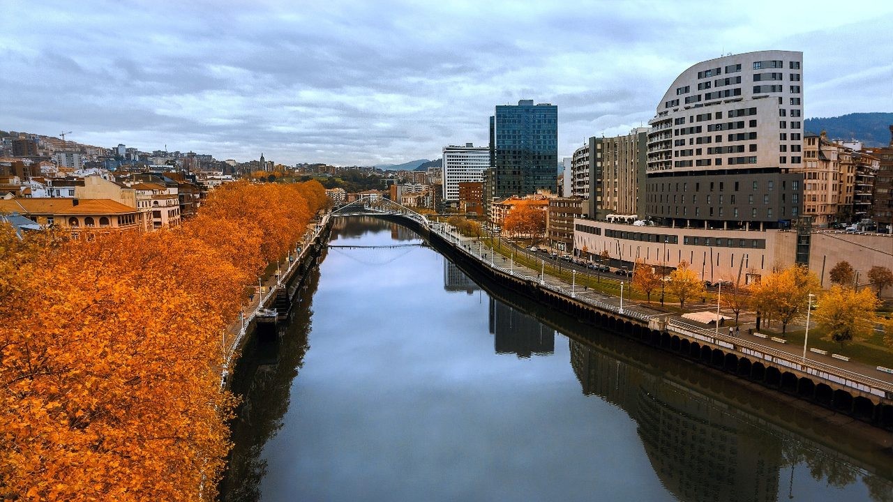 Rivier de Nervión in Bilbao met herfstbladeren en de Zubizuri-brug op de achtergrond tijdens een roadtrip door Noord-Spanje.